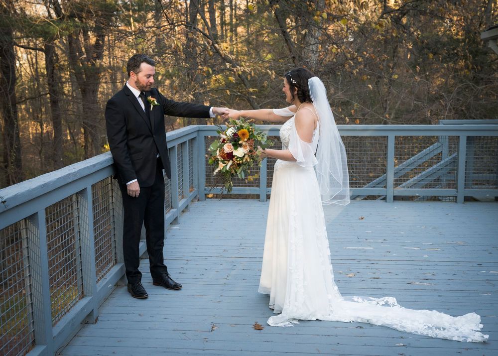 A wedding couple poses on a wooden deck surrounded by autumn trees during their outdoor ceremony.
