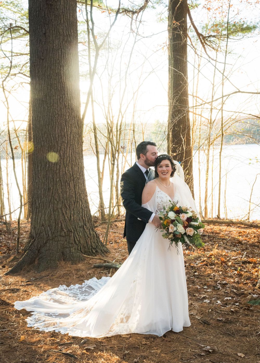 A romantic wedding photo session in a wooded area with fallen autumn leaves.
