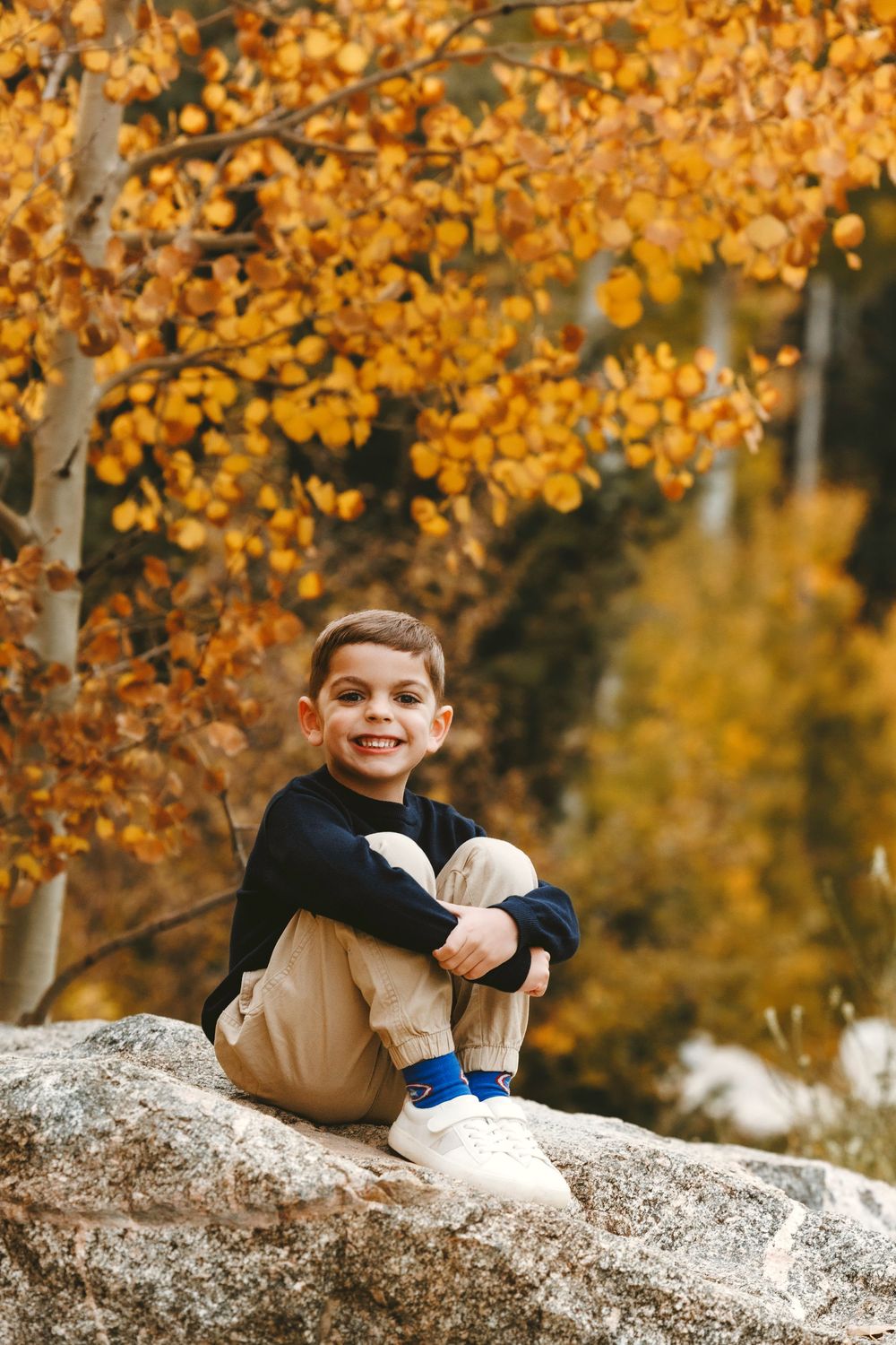 Happy young boy sitting on a rock surrounded by vibrant golden autumn foliage.