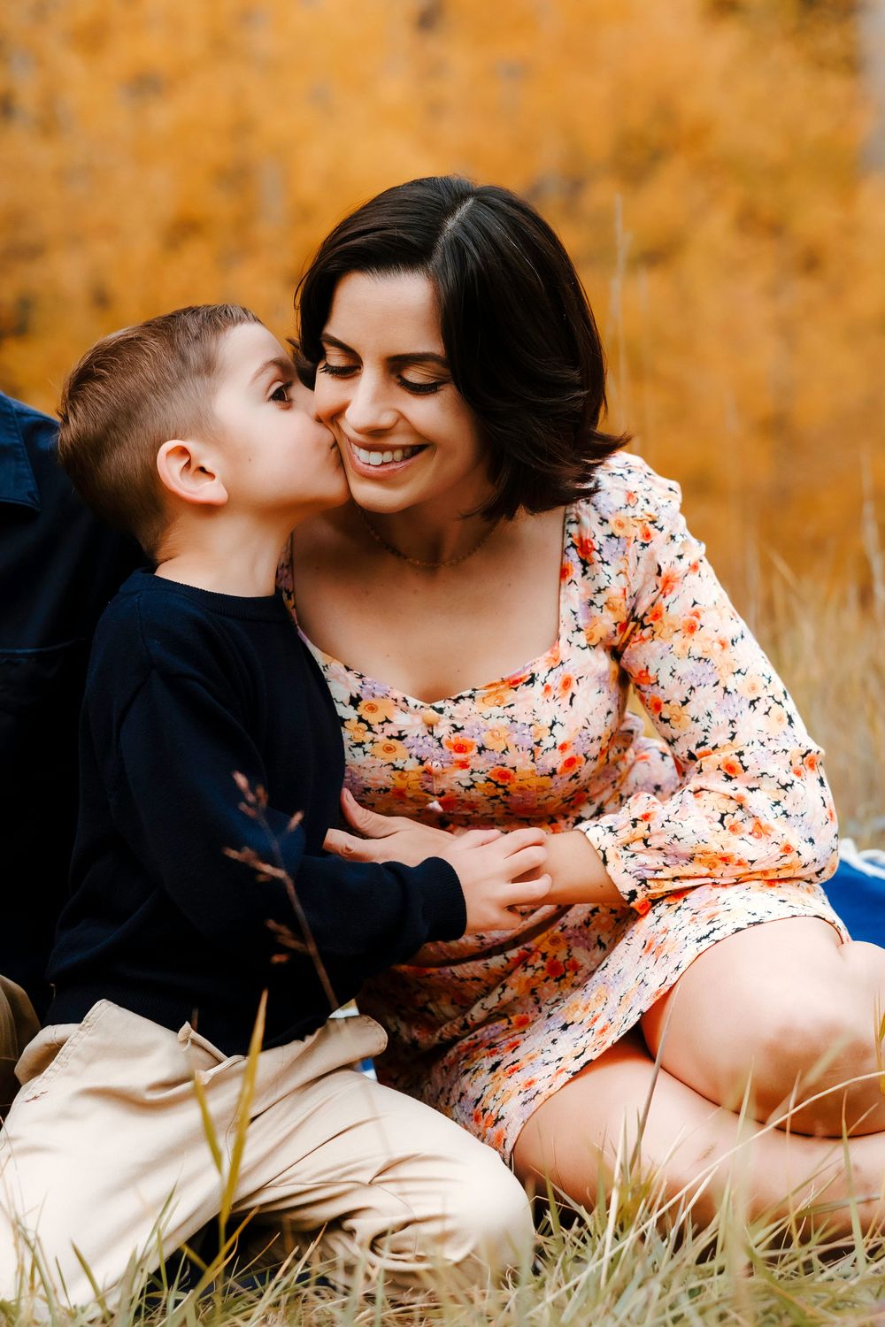 Smiling mother receiving a kiss on the cheek from her young son in fall foliage.