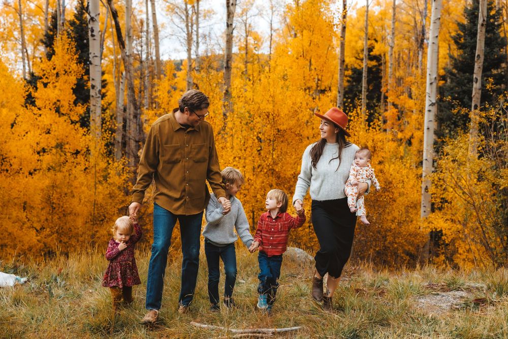 Happy family of five walks hand-in-hand through a stunning golden aspen forest in fall.