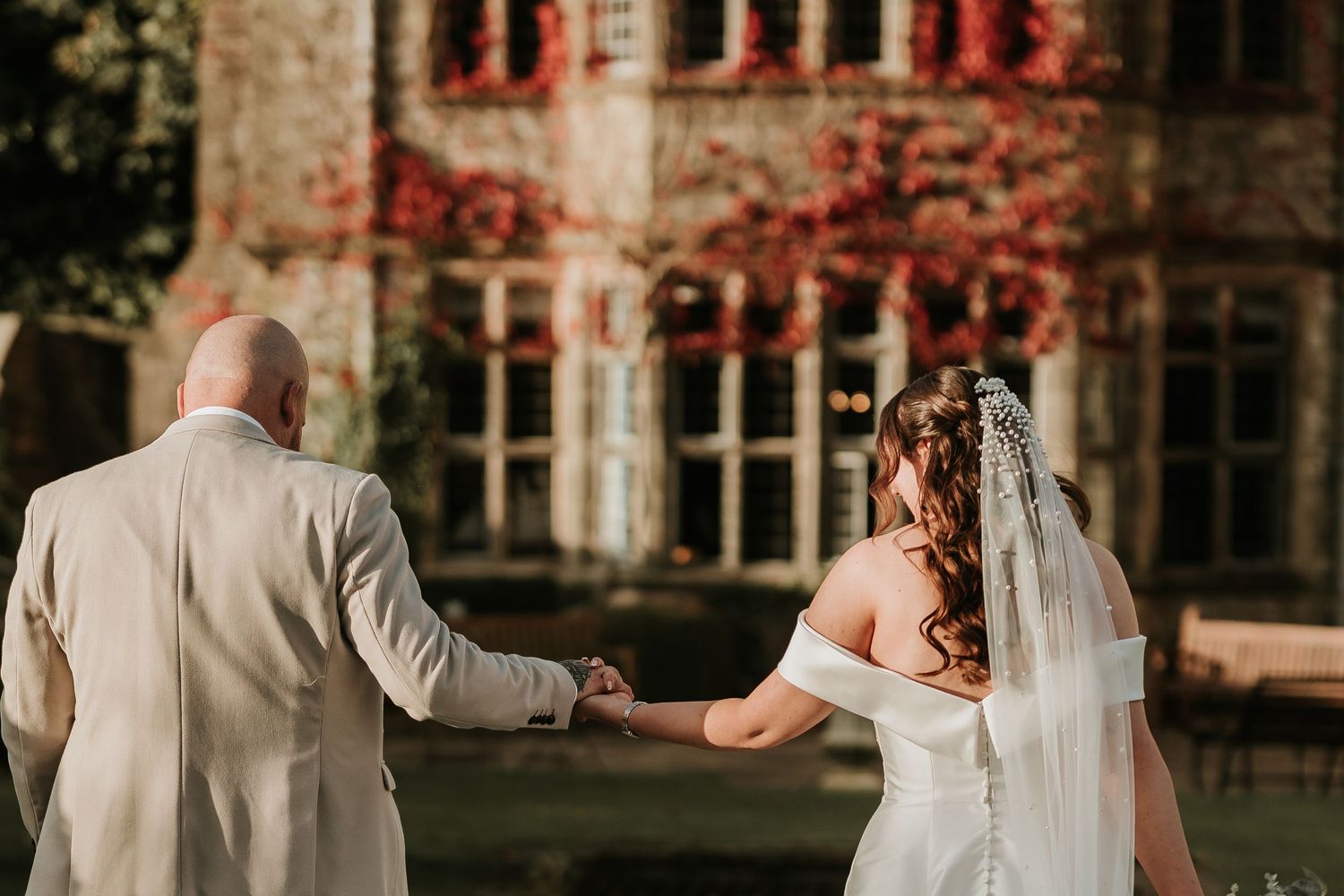 A romantic wedding couple shares intimate moments in a garden setting with autumn foliage and historic architecture.