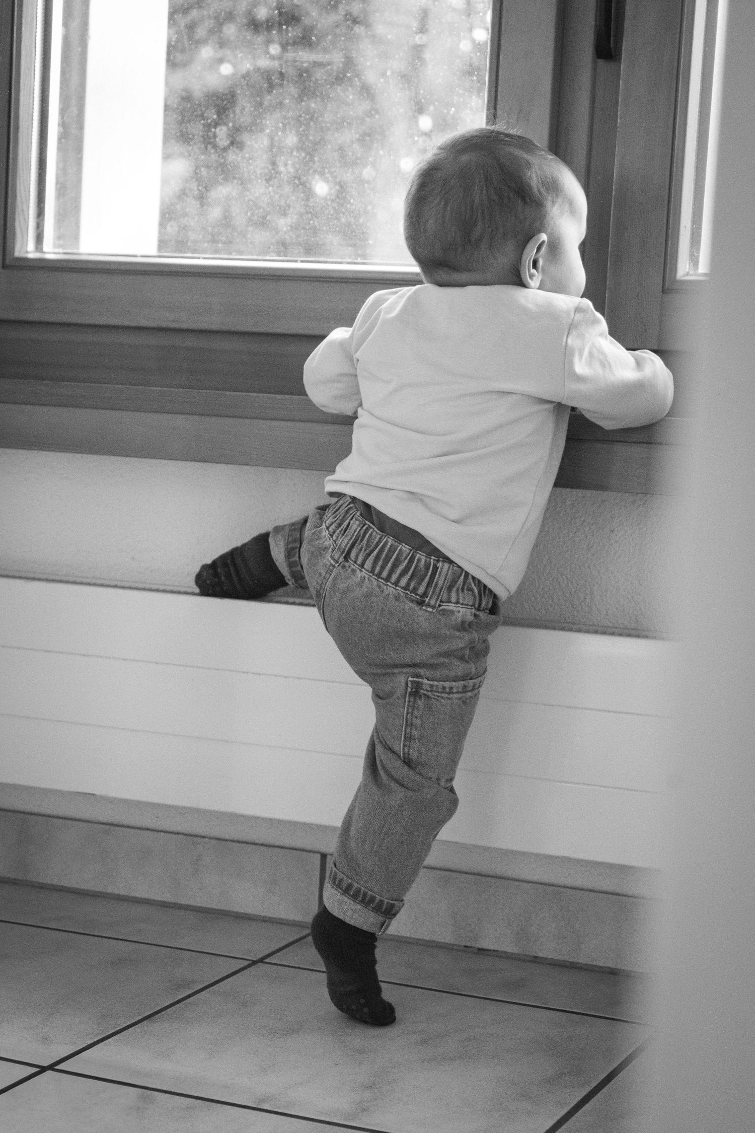 Black and white sequence of toddler climbing up to peek through window.