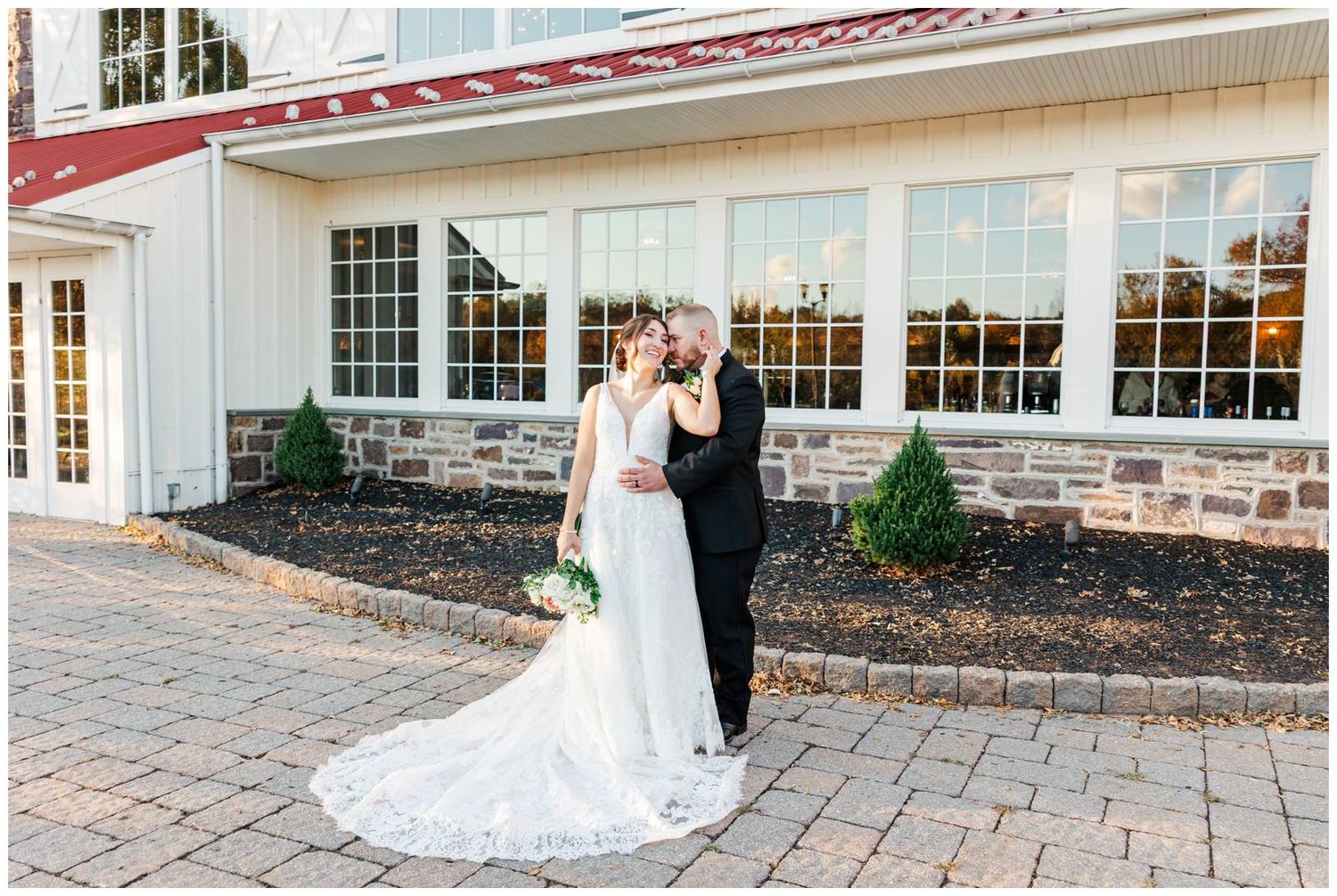 Exterior view of a white wedding venue with large windows and stone patio.