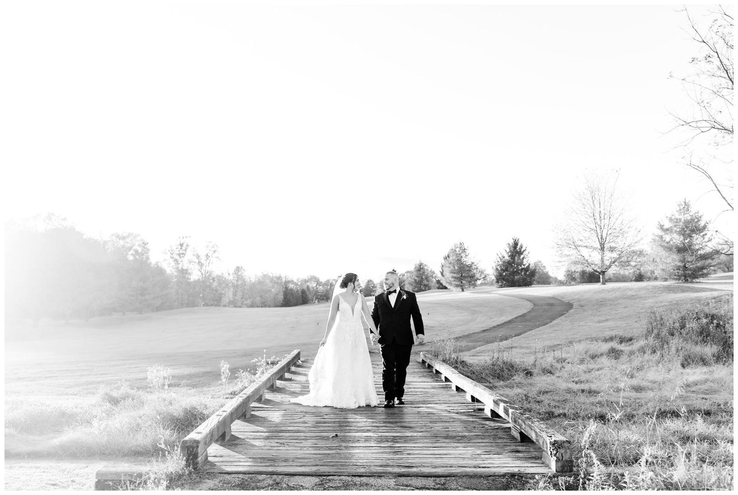Two silhouetted figures walk along a misty pathway through a rural landscape in black and white.