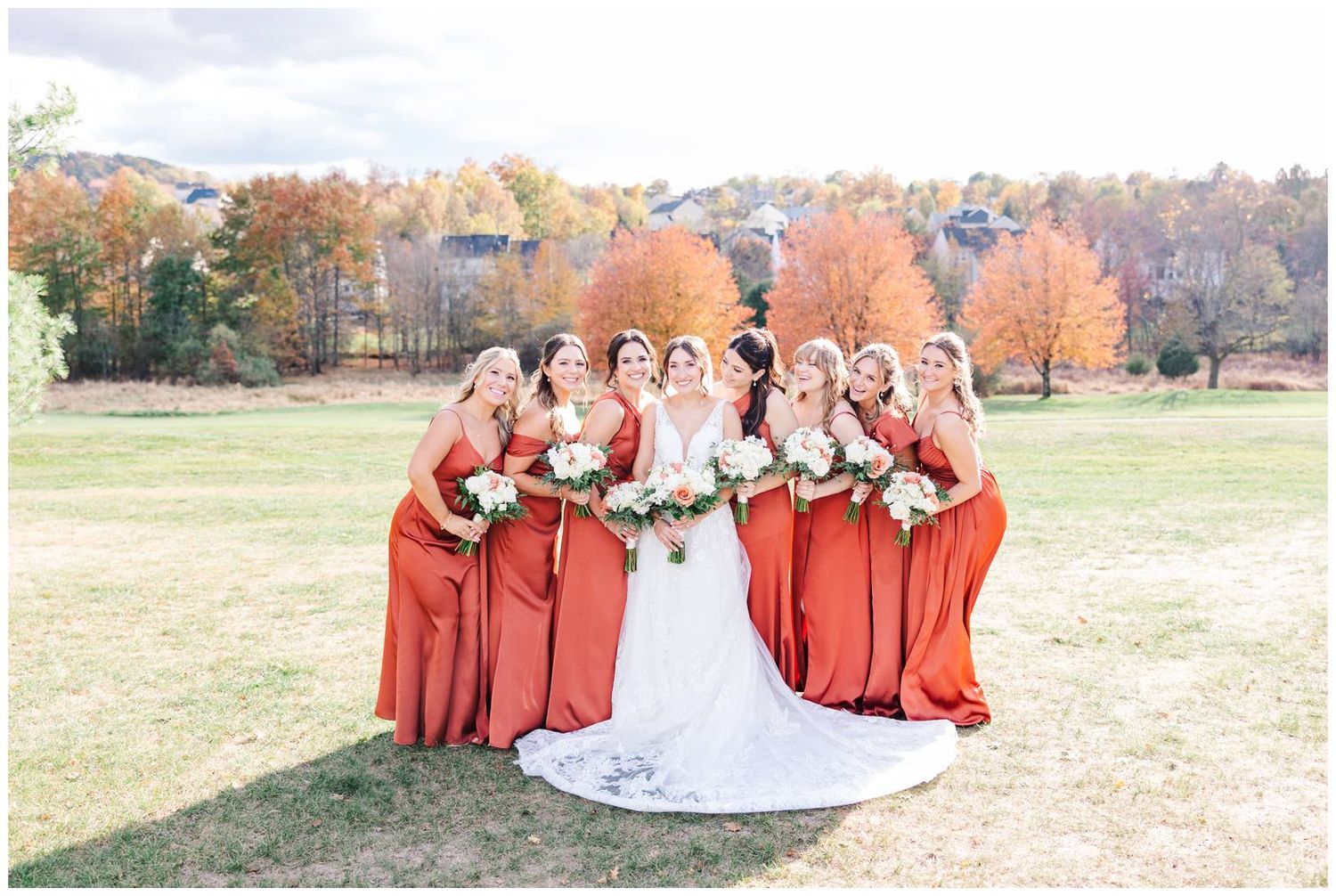 Wedding party in autumn with bridesmaids wearing rust-colored dresses against fall foliage.