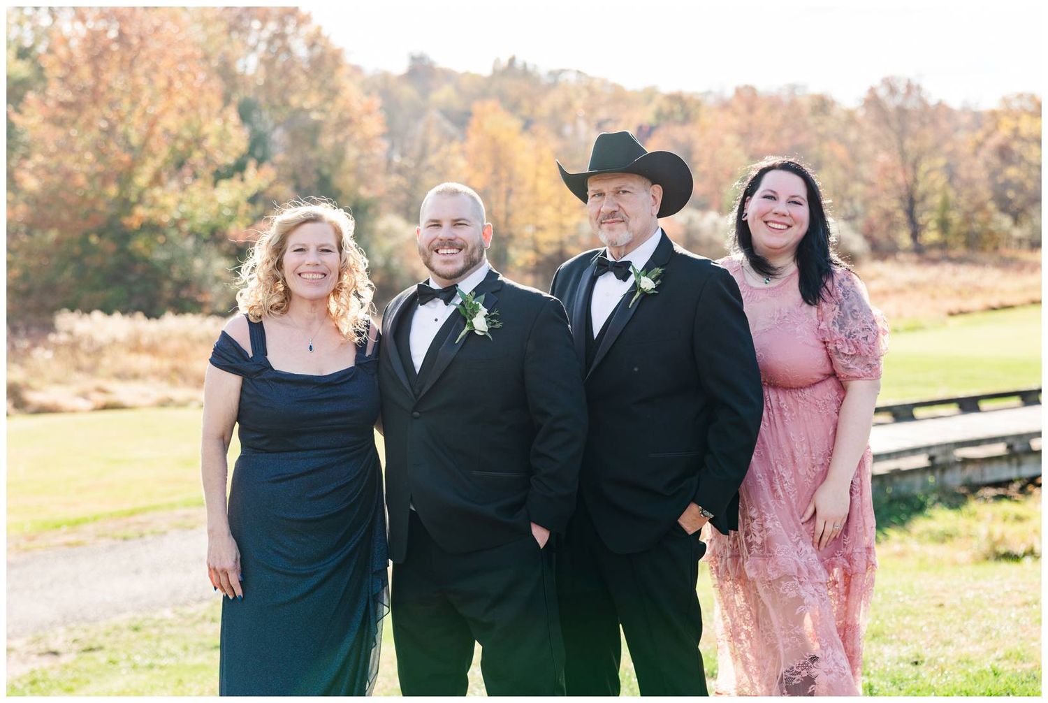 A group of people stand together outdoors in formal attire during an autumn day.