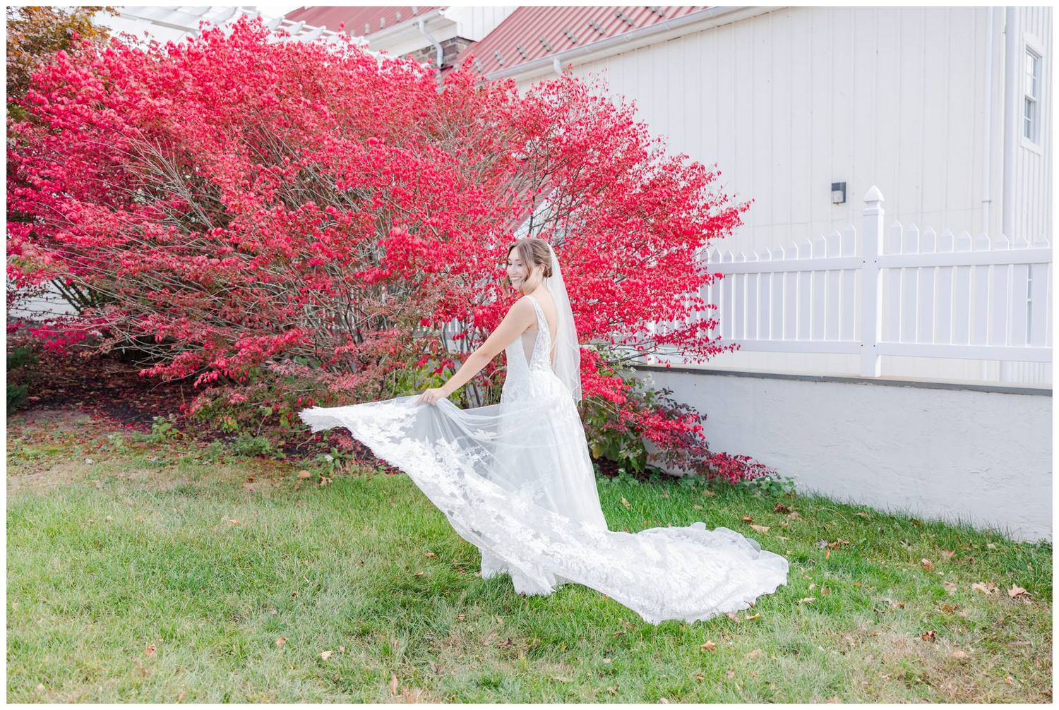 White wedding dress flowing in the wind against vibrant red autumn foliage and white building backdrop.