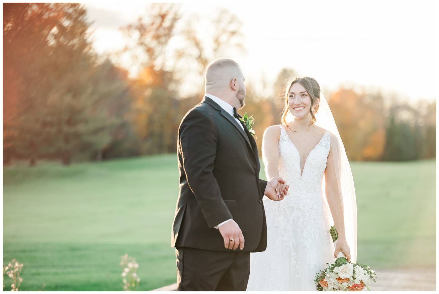 Elegant wedding couple poses in golden sunset light on a grassy field during their autumn celebration.