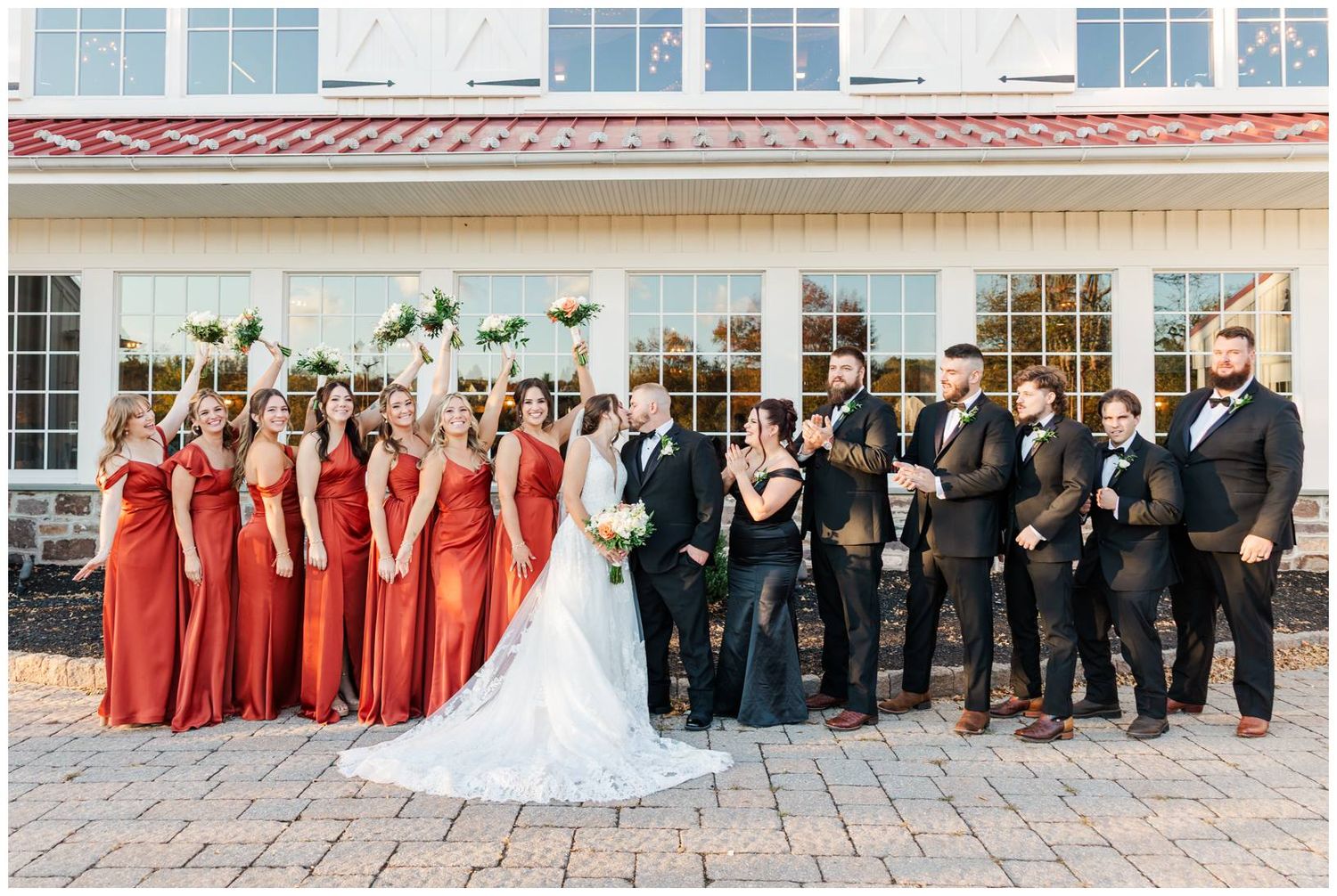 A wedding party in formal attire poses together outside a building with red and black color coordination.