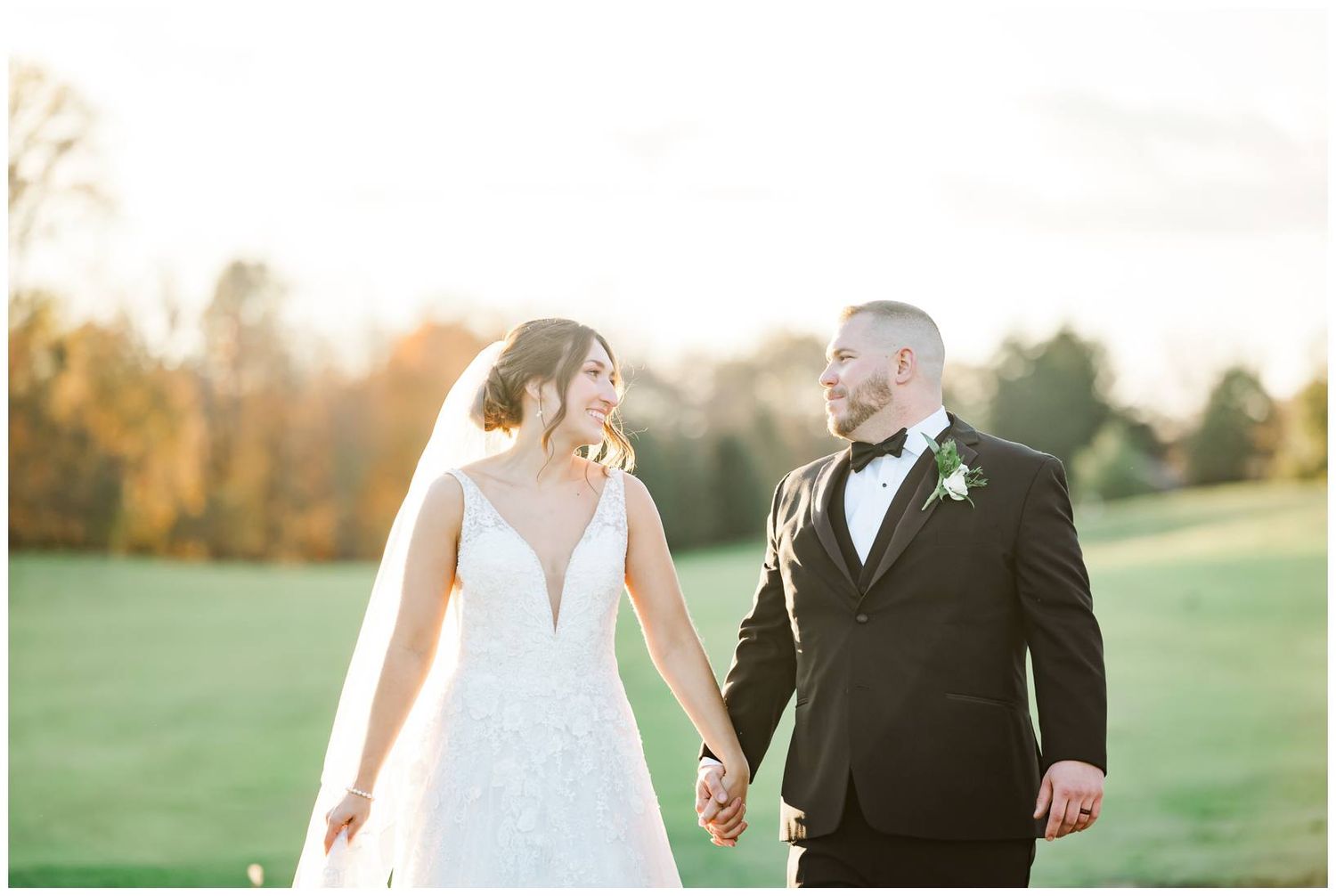 Romantic sunset portraits of newlyweds walking together in golden light on grassy field.