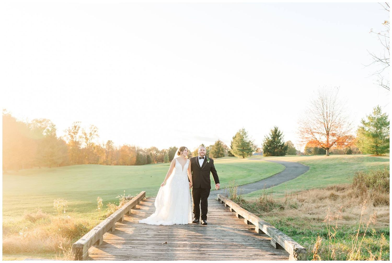 A couple walks along a wooden boardwalk path during golden hour at a golf course.