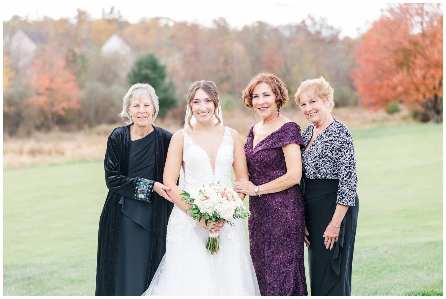 Wedding party members in formal attire pose together during autumn with colorful fall foliage.