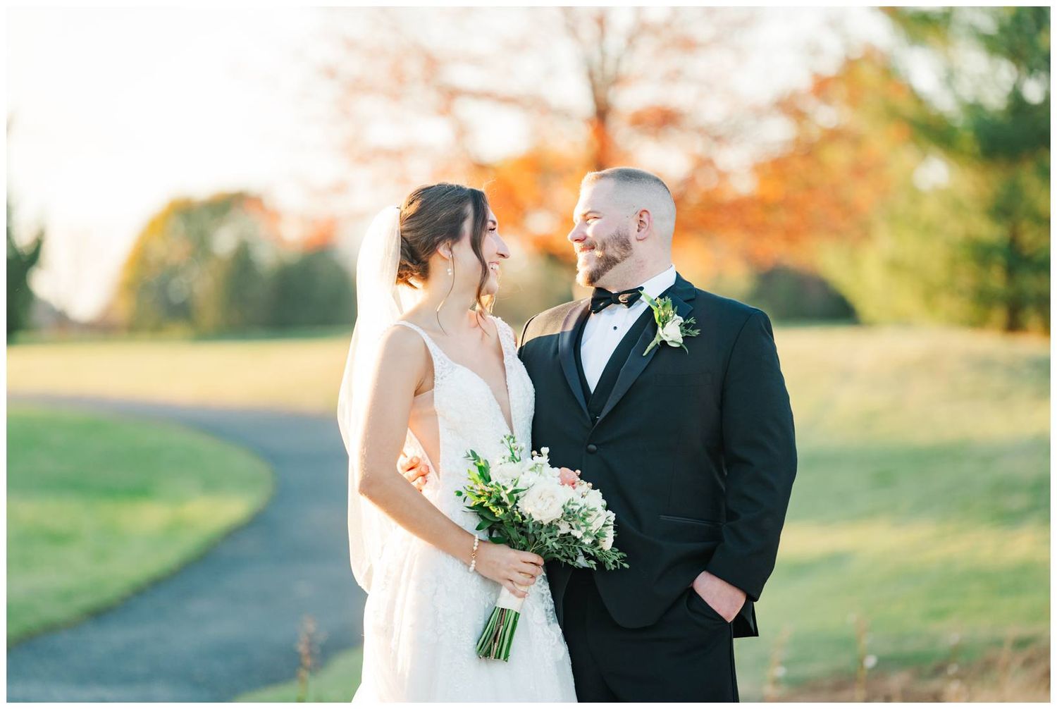 Elegant wedding couple poses outdoors during golden hour with autumn foliage in the background.