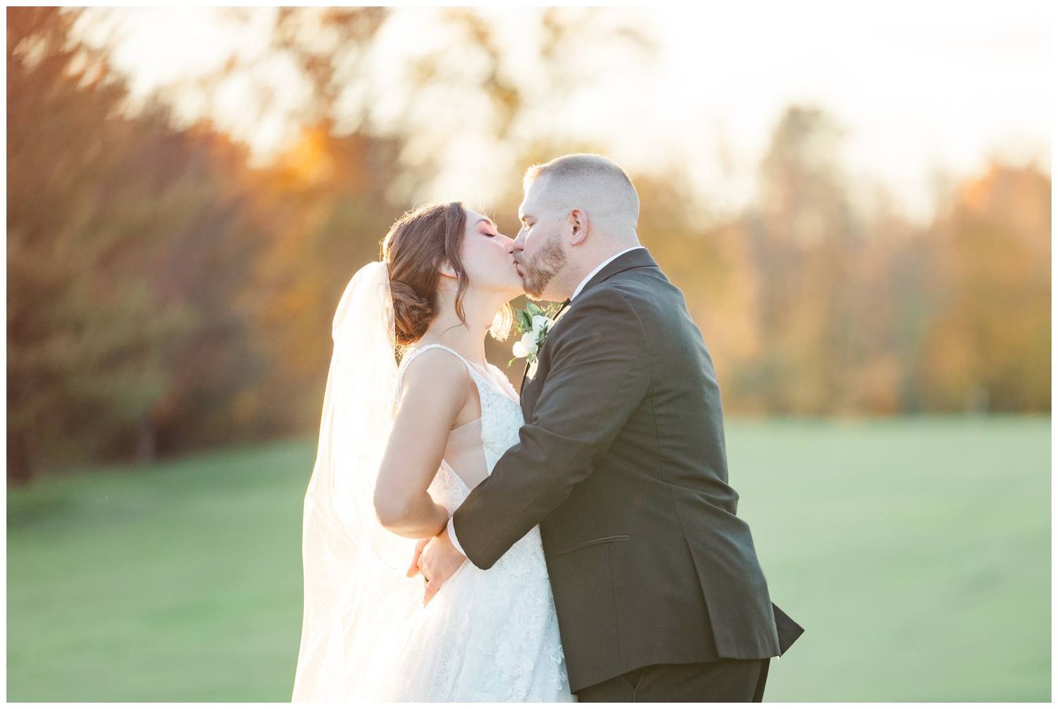 Intimate wedding couple embraces during golden hour sunset in an open field.