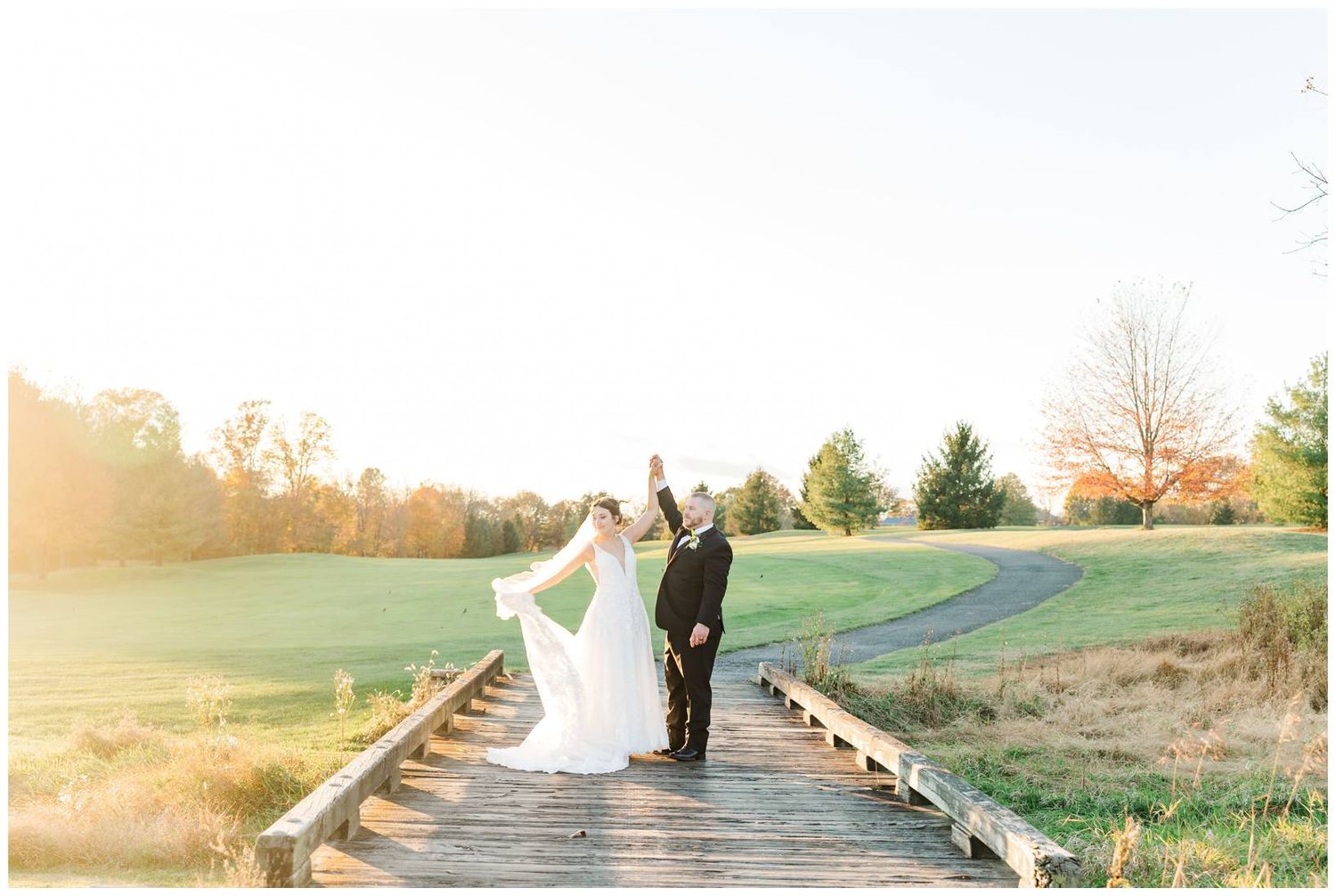Wedding party walking through a scenic field at sunset with golden light filtering through trees.
