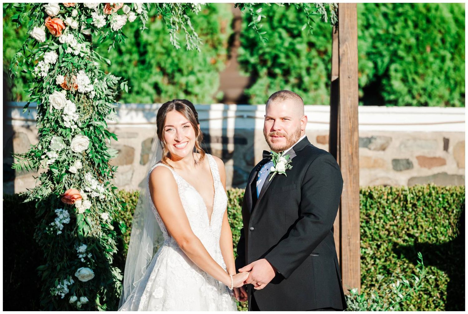 Wedding couple and wedding party posing for formal photos in front of lush greenery.