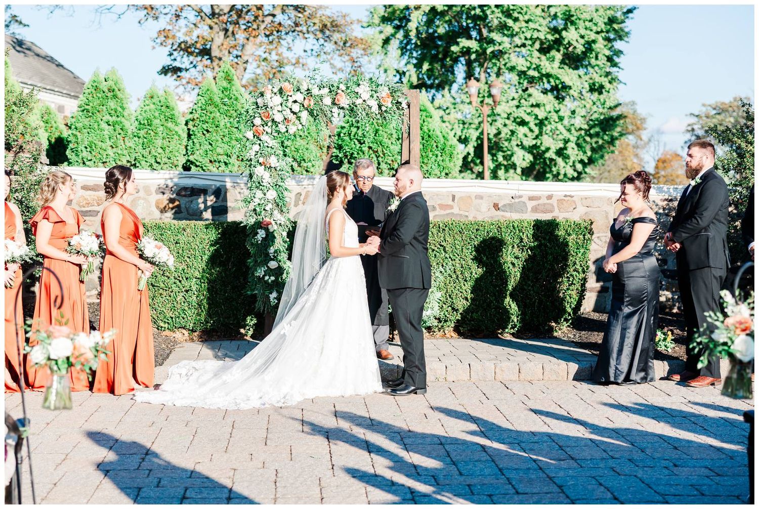 Wedding ceremony guests gathered on an outdoor stone patio surrounded by lush greenery.