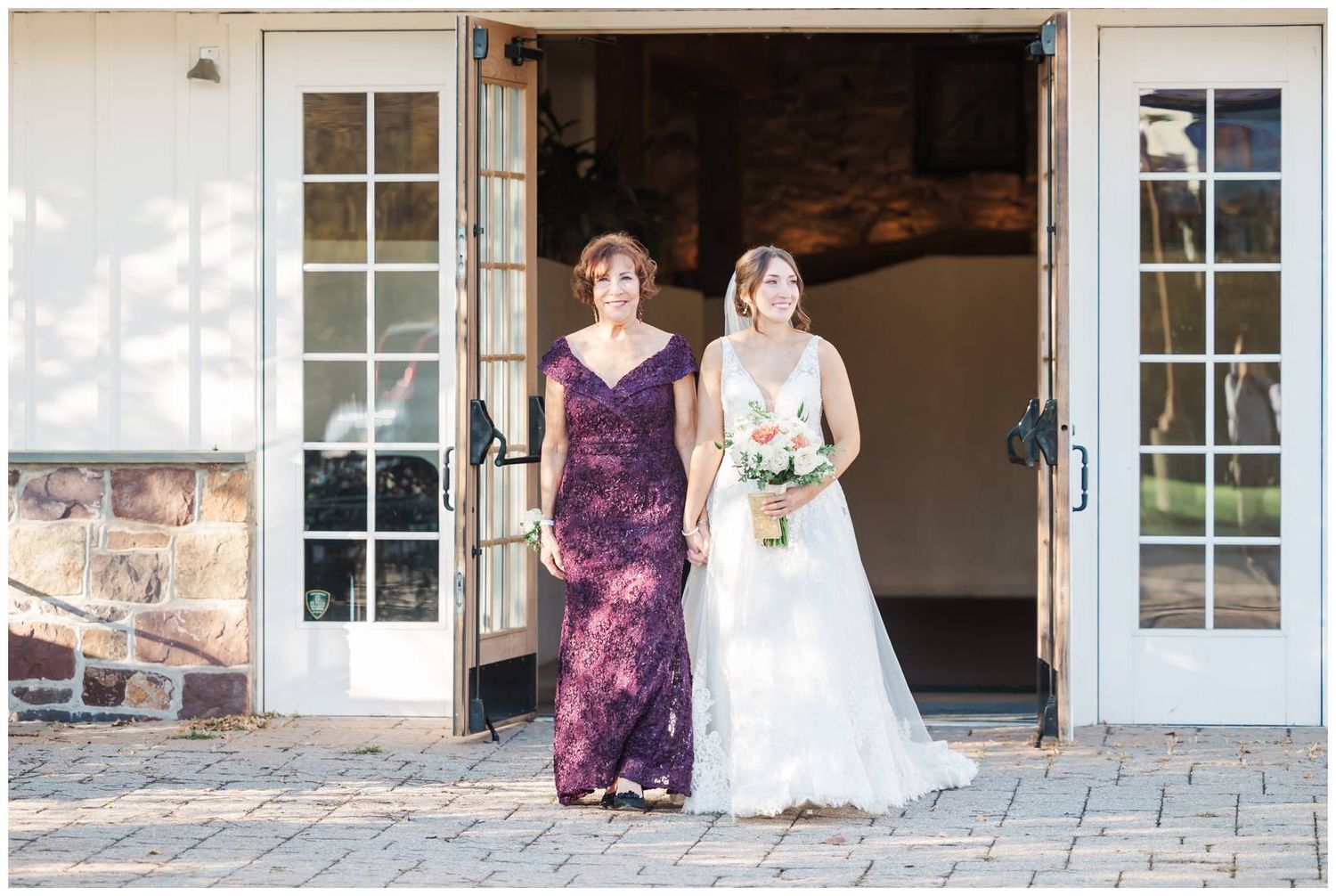 Wedding party members posing in front of white French doors on a stone patio.