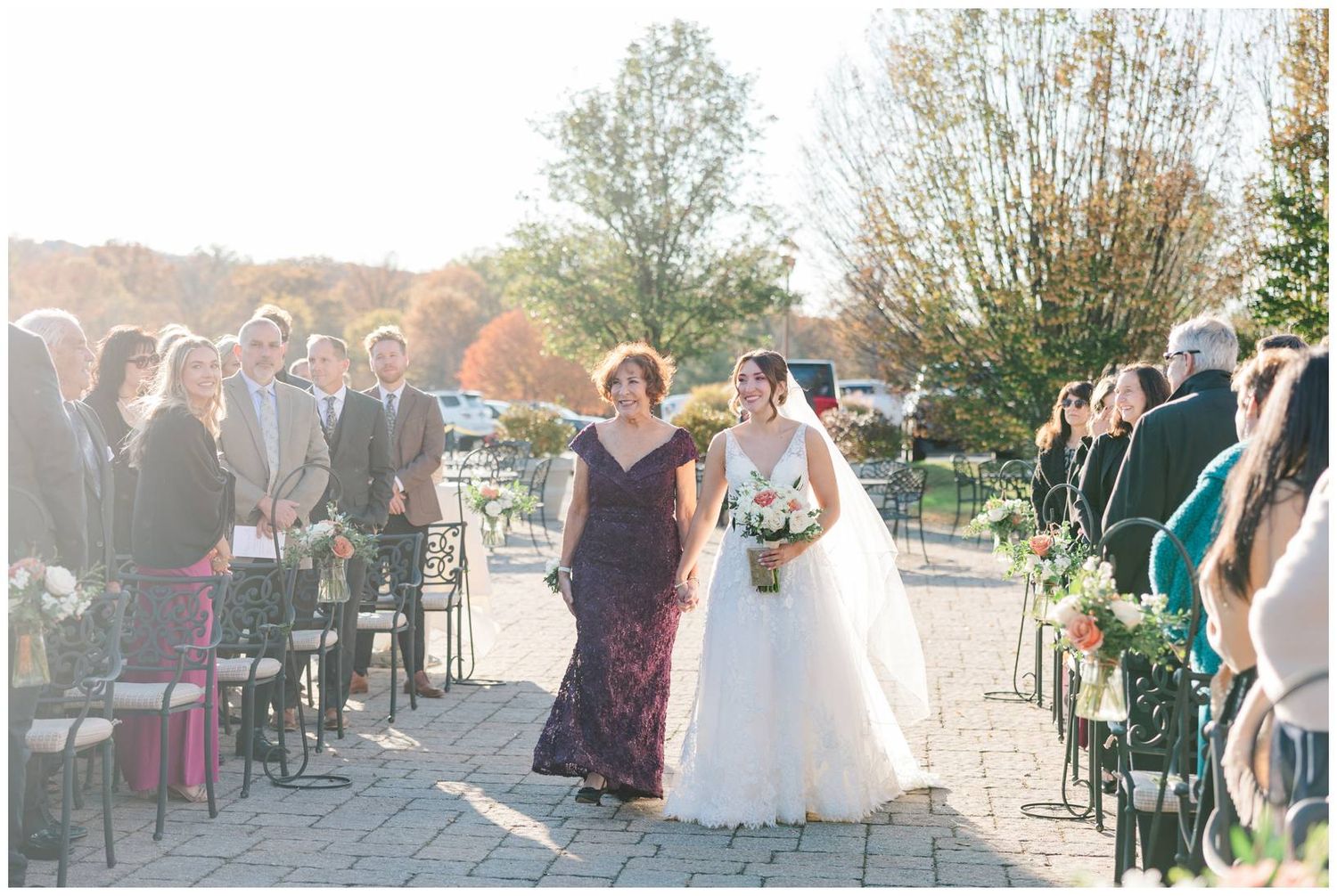 Outdoor wedding ceremony setup with white chairs and guests gathered on a sunny day.
