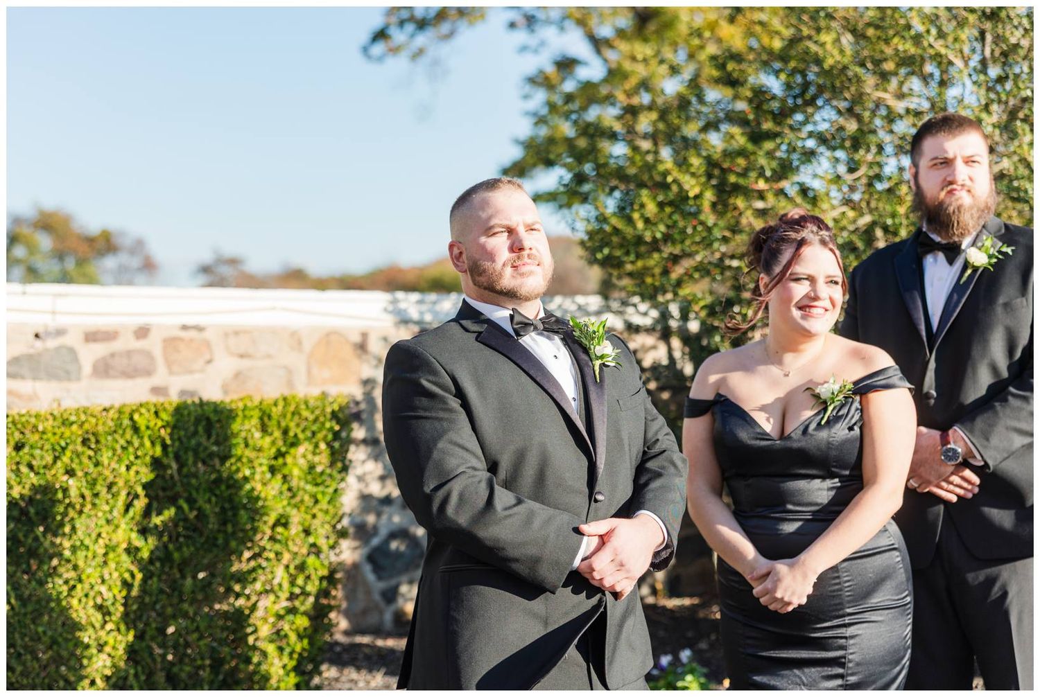 Outdoor wedding ceremony with couple and officiant standing against manicured hedge backdrop.