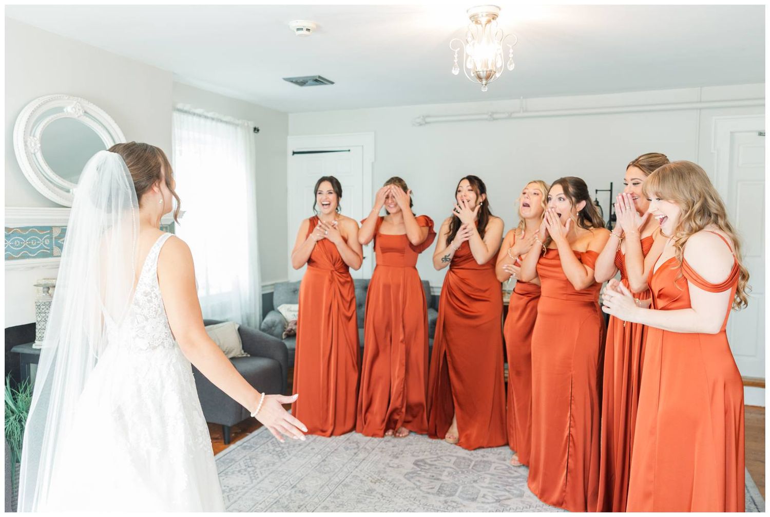 Bridesmaids in matching rust-colored dresses react emotionally during a wedding first look reveal.