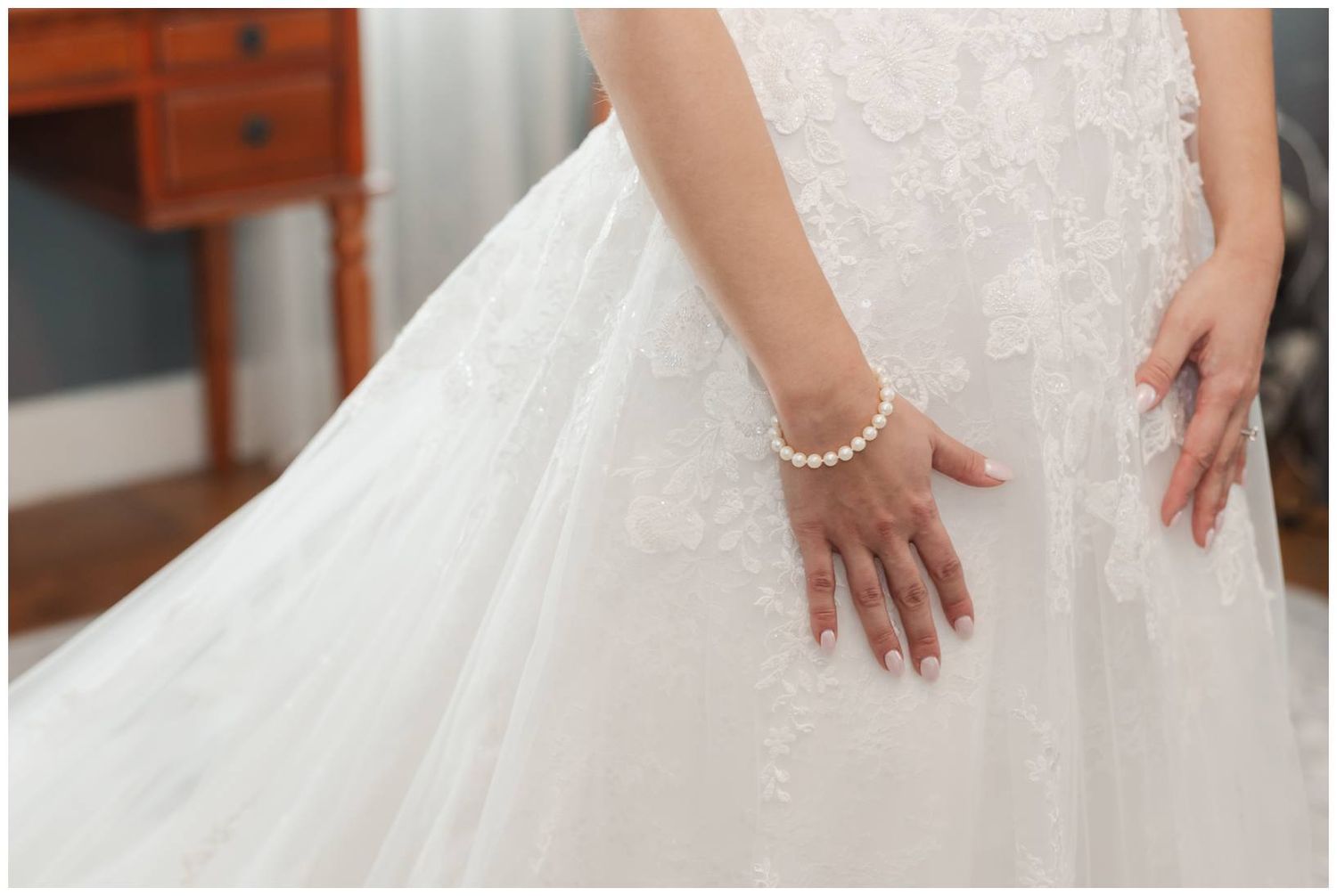 Close-up details of a bride's hands and wedding dress showing delicate lace, pearls, and elegant styling.
