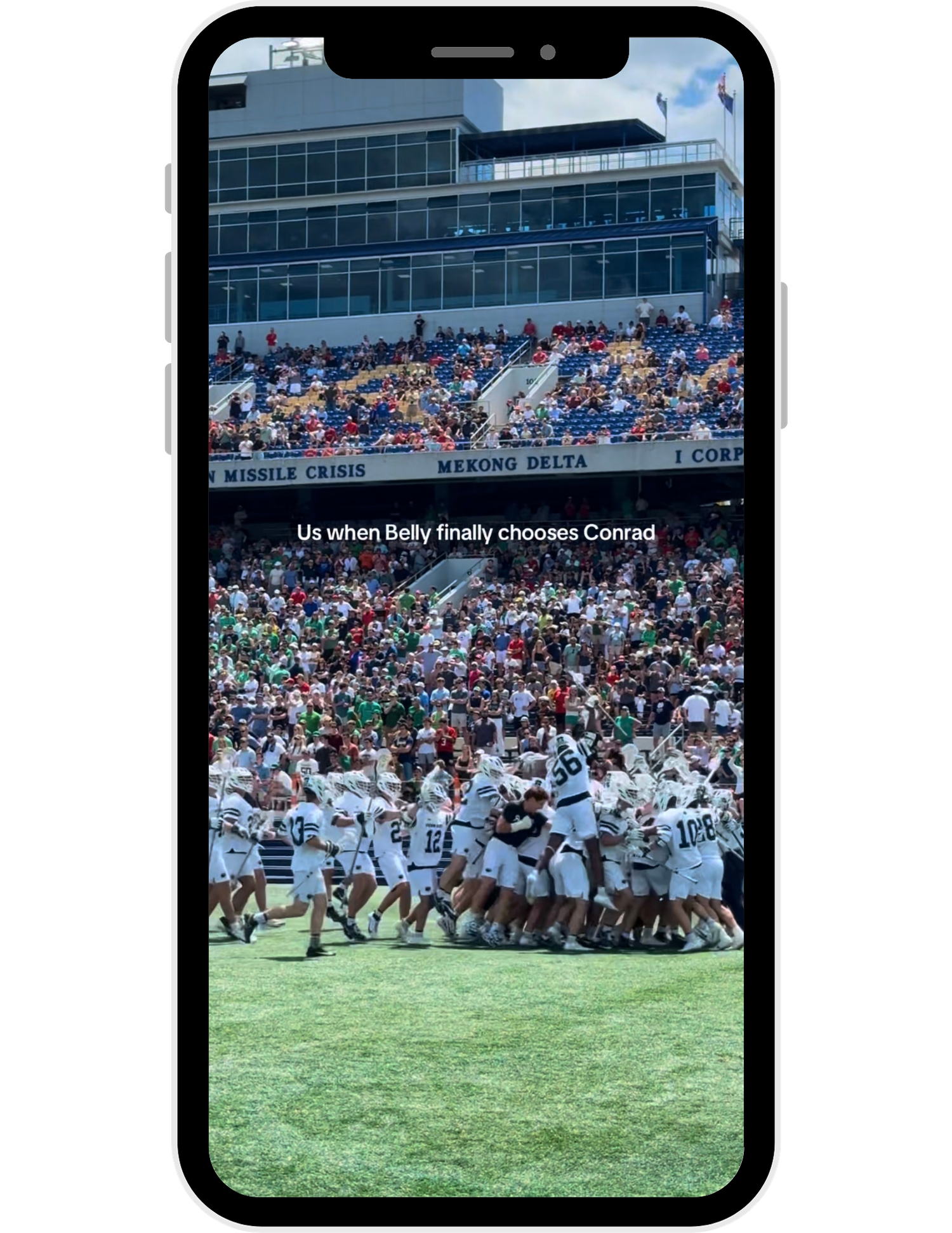 Rugby players engage in a scrum formation during a match on a grass field with spectators in the stands.