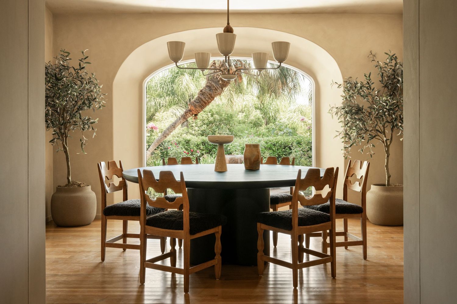 Elegant dining room with arched windows, wooden chairs, and pendant lighting illuminating a long table in warm tones.