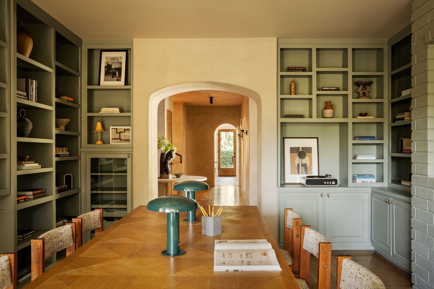 Long hallway with built-in bookshelves and arched doorways features sage green walls and hardwood flooring.
