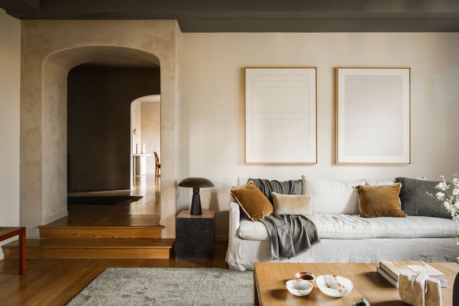 Modern minimalist living room interior with beige sofa, wooden furniture and arched doorway in neutral tones.