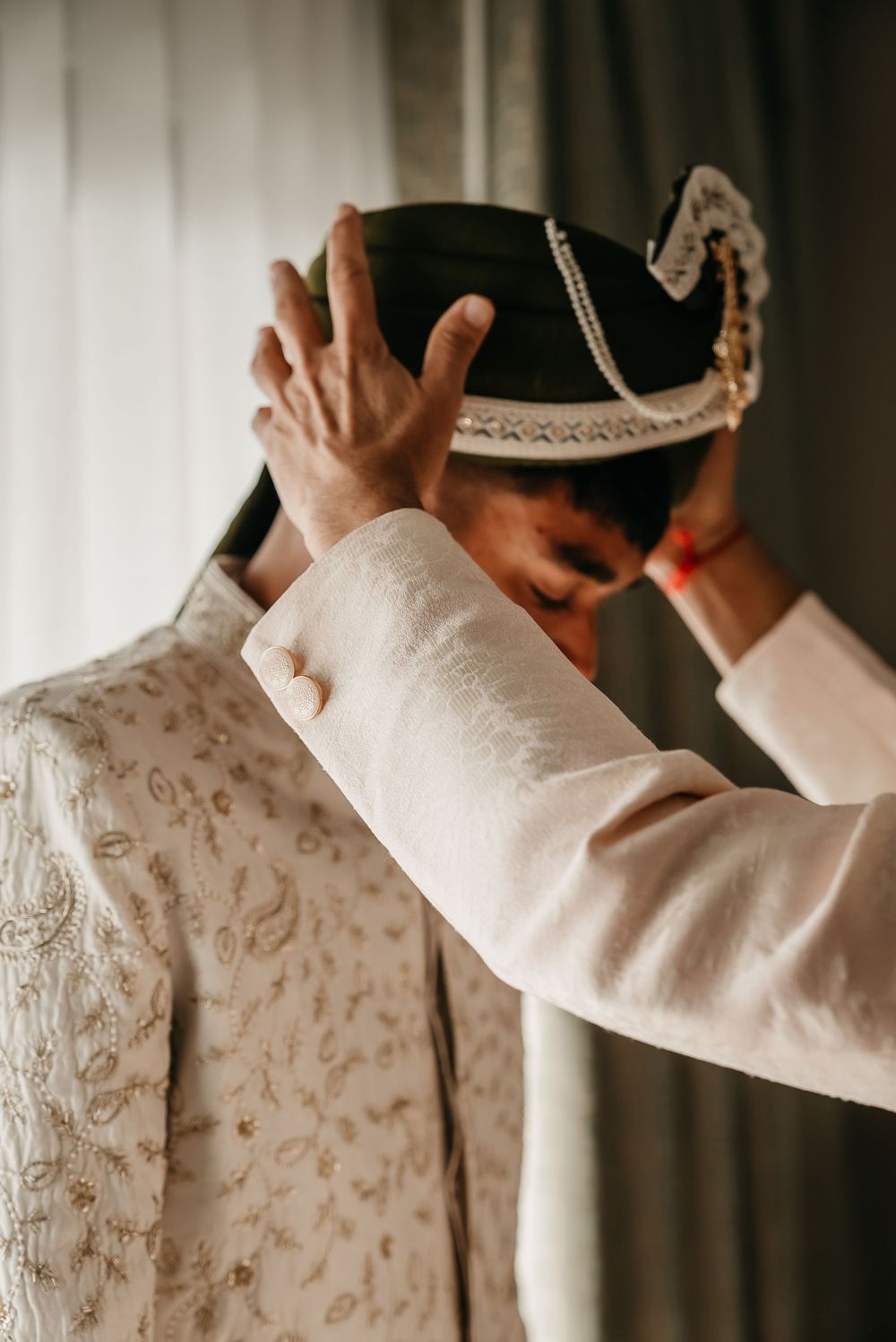 Someone adjusts a decorative black tricorn hat while wearing an ornate white embroidered jacket.