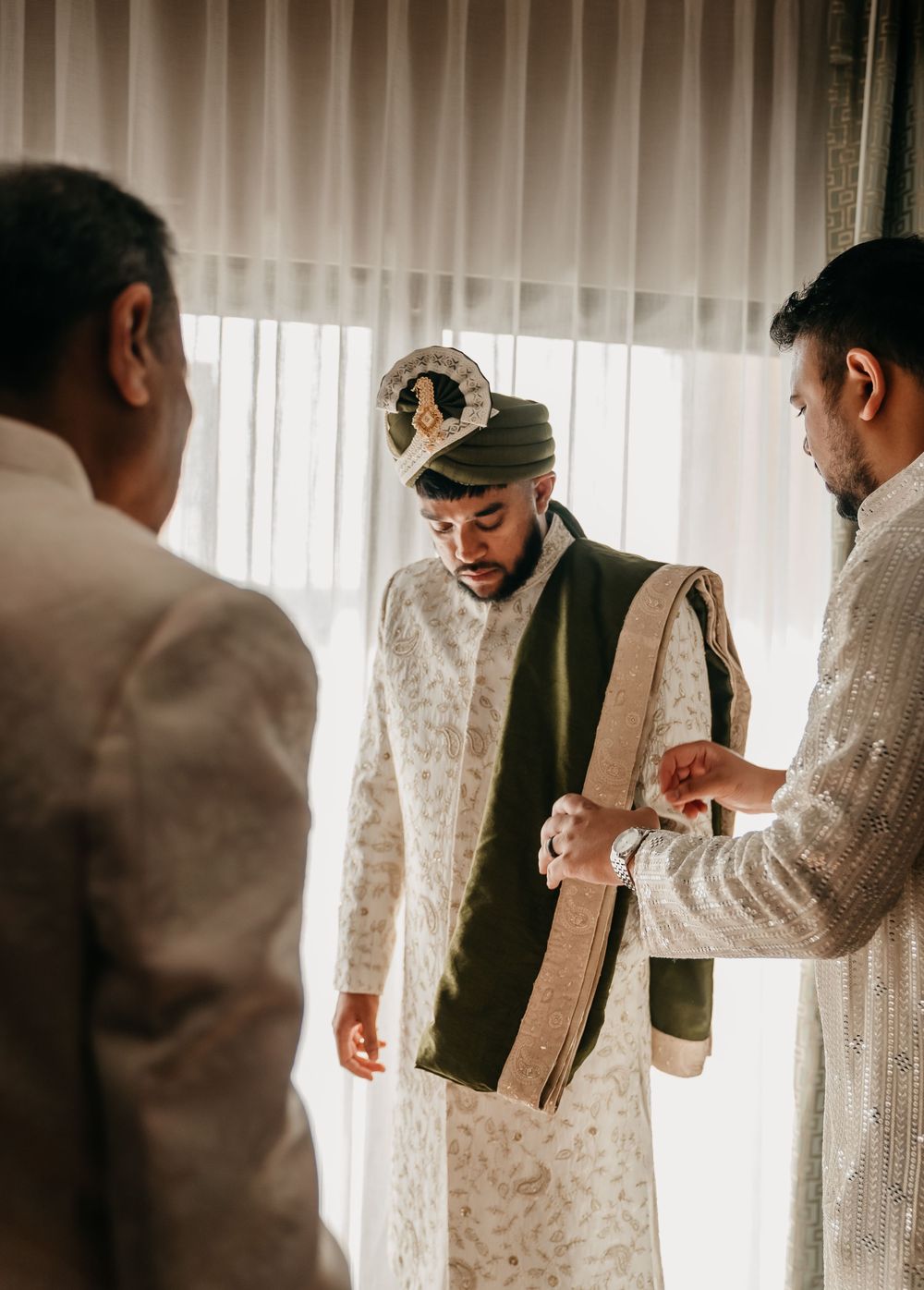 A sequence of five photos showing a couple getting ready in a sunlit room with white curtains and elegant attire.