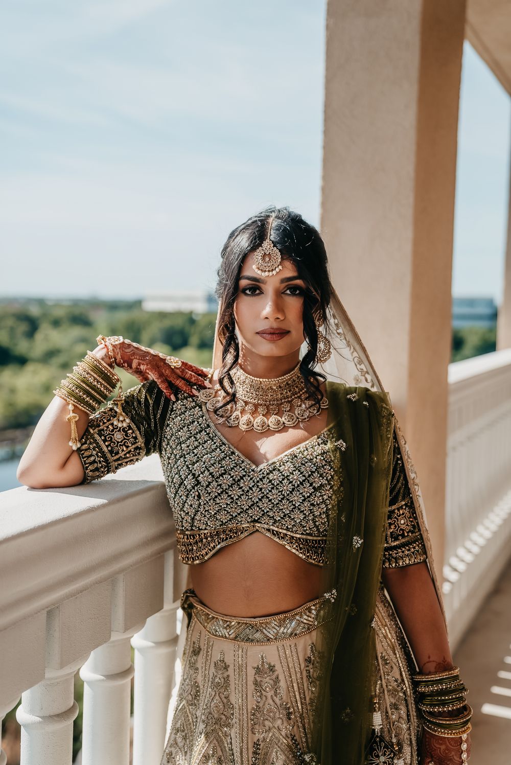 Traditional South Asian bridal attire featuring intricate beadwork, jewelry and a flowing lehenga on an elegant balcony.