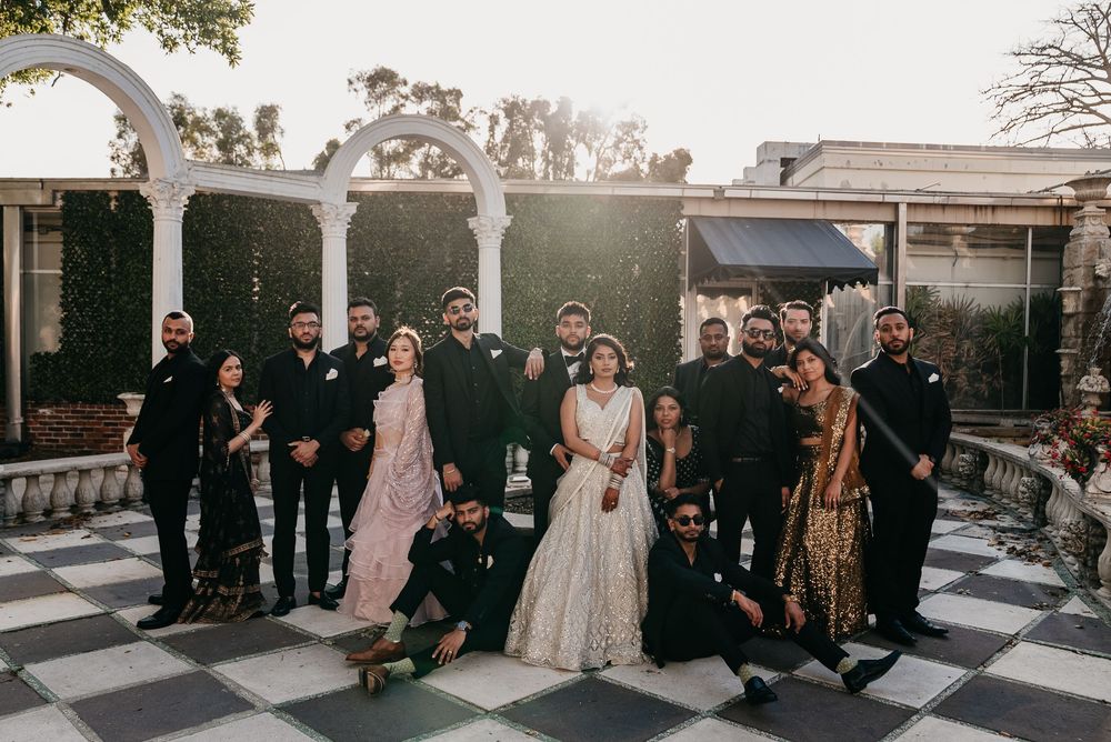 Wedding party poses together on a black and white checkered patio at sunset with decorative arch in background.