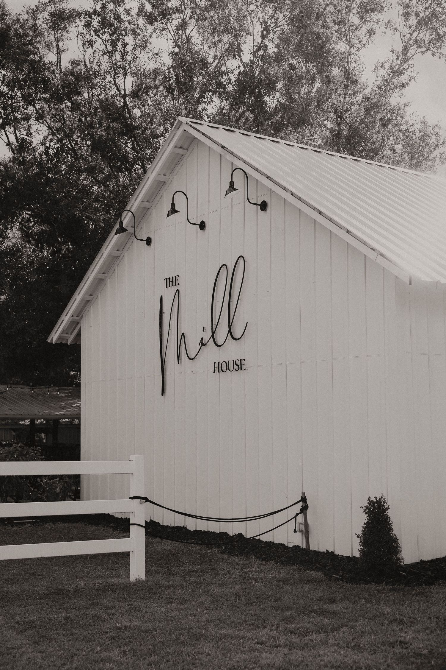 Black and white photograph of The Mill House barn venue with modern signage.
