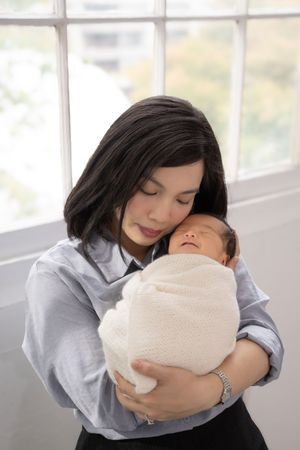 A tender moment showing a parent in a gray shirt embracing and cradling a newborn baby wrapped in a cream blanket.