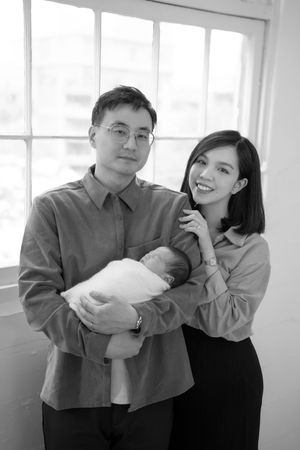 Black and white photo series showing a couple holding and admiring their newborn baby in a bright interior space.
