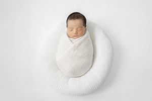 A creative photo sequence showing a baby wrapped in white swaddling cloth gradually rotating in a circle against white background.