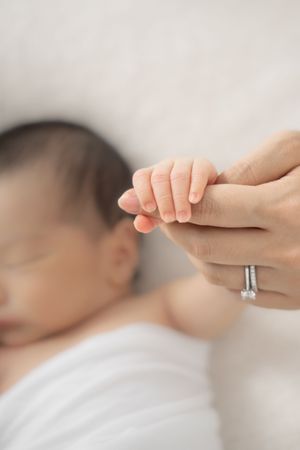 Close-up view of a tiny newborn baby's hand grasping an adult finger against a white background.
