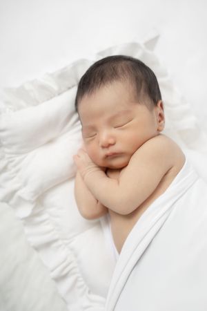 Peaceful newborn baby sleeping soundly wrapped in soft white blanket on white background.