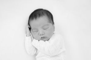 A sleeping newborn baby swaddled in white blankets rests peacefully against a white background.