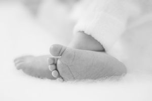 Close-up black and white photo of a newborn baby's tiny feet against a soft white background.