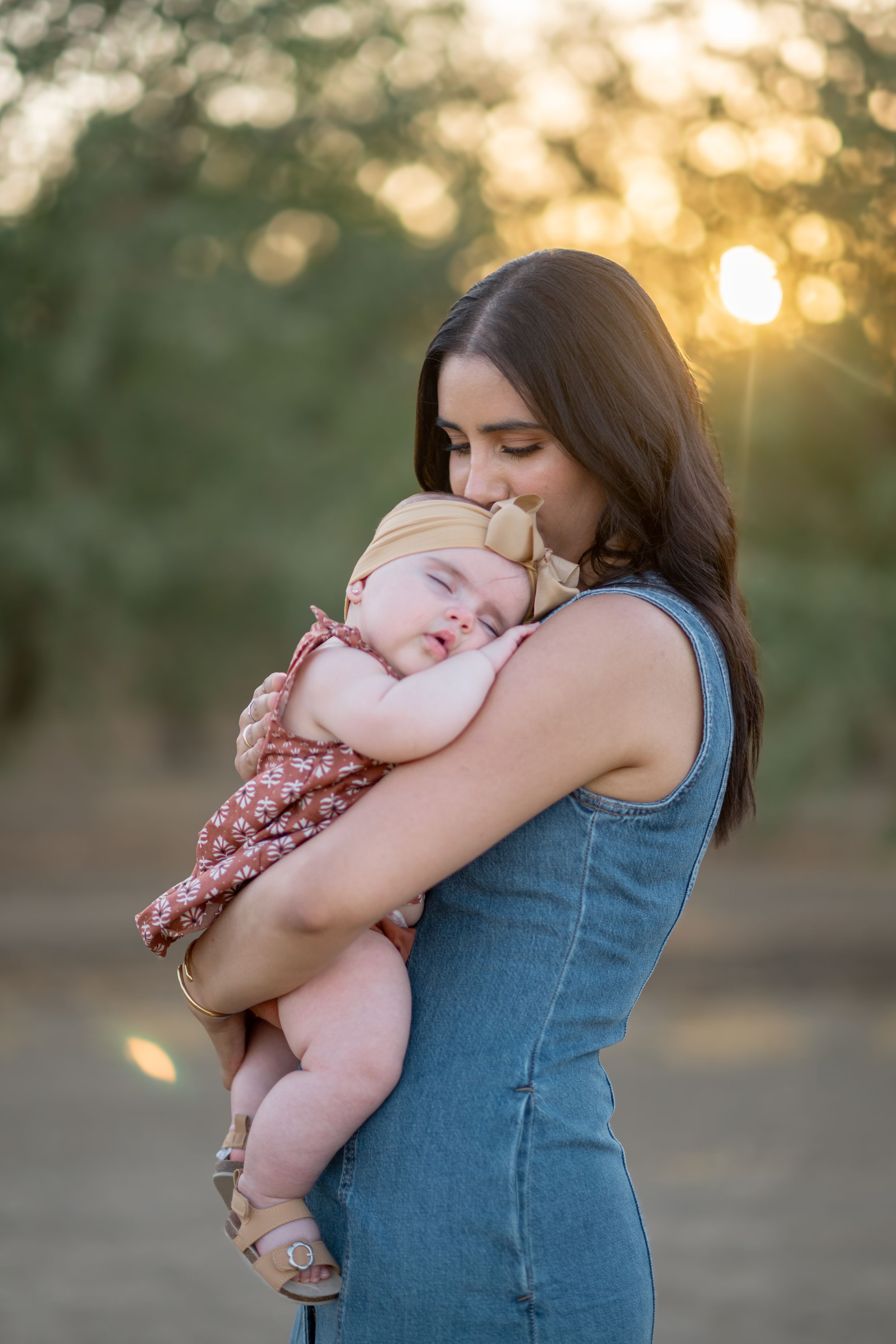 A tender moment captured as someone cradles and kisses a baby against a sunset backdrop.