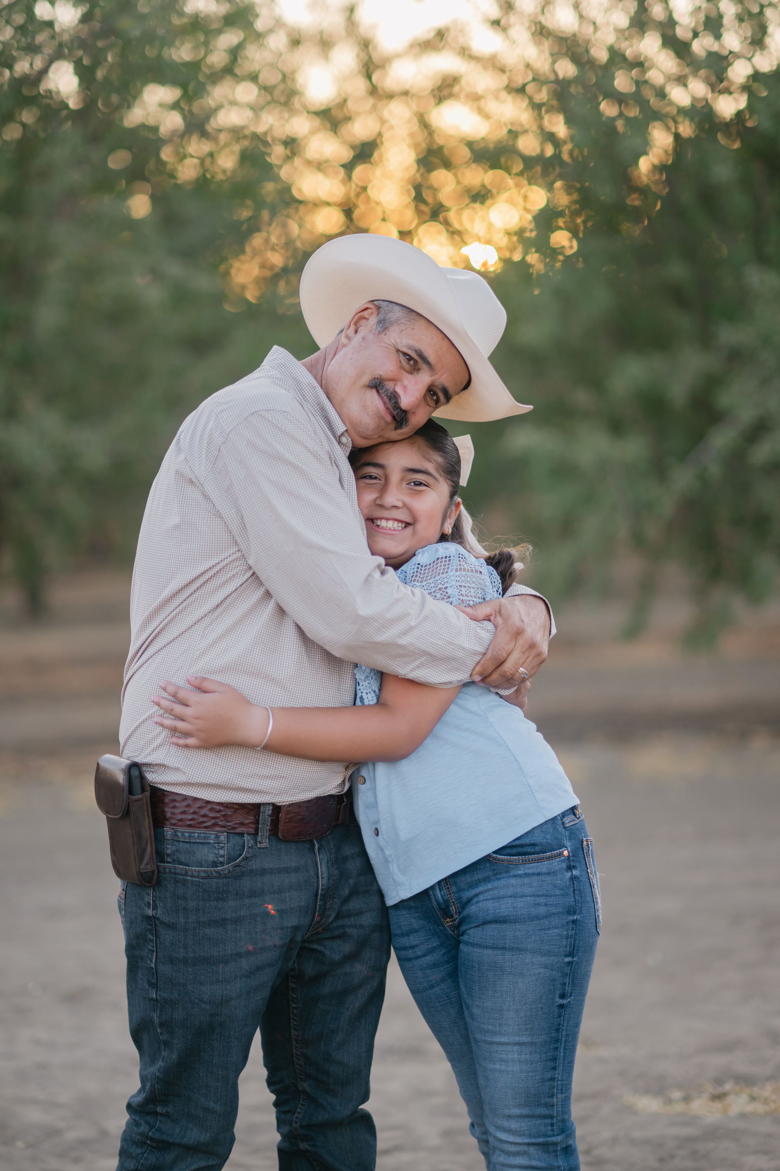 A heartwarming embrace between two people wearing jeans captured at sunset in an orchard setting.
