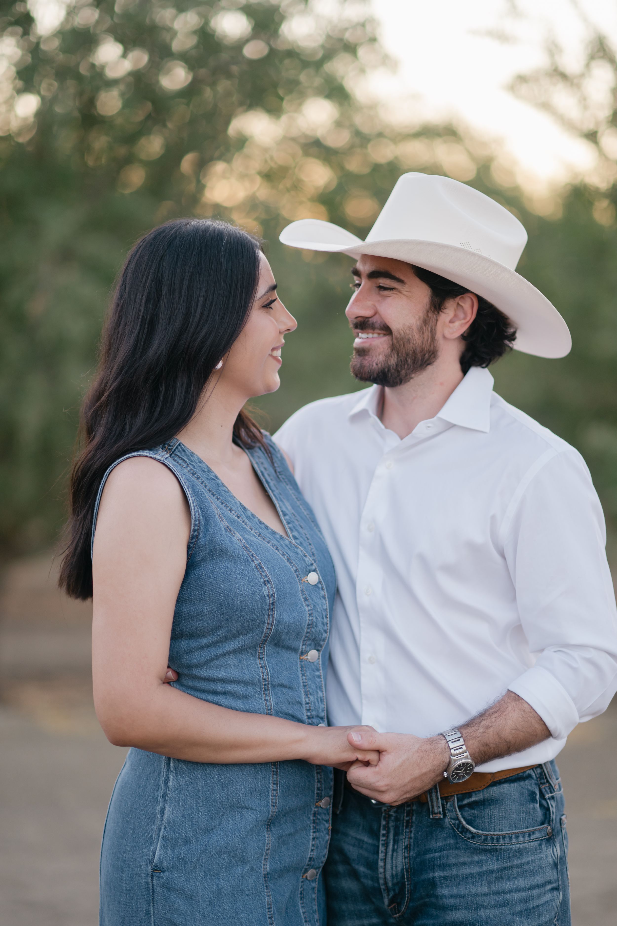 A couple in western attire shares a romantic moment outdoors during golden hour.