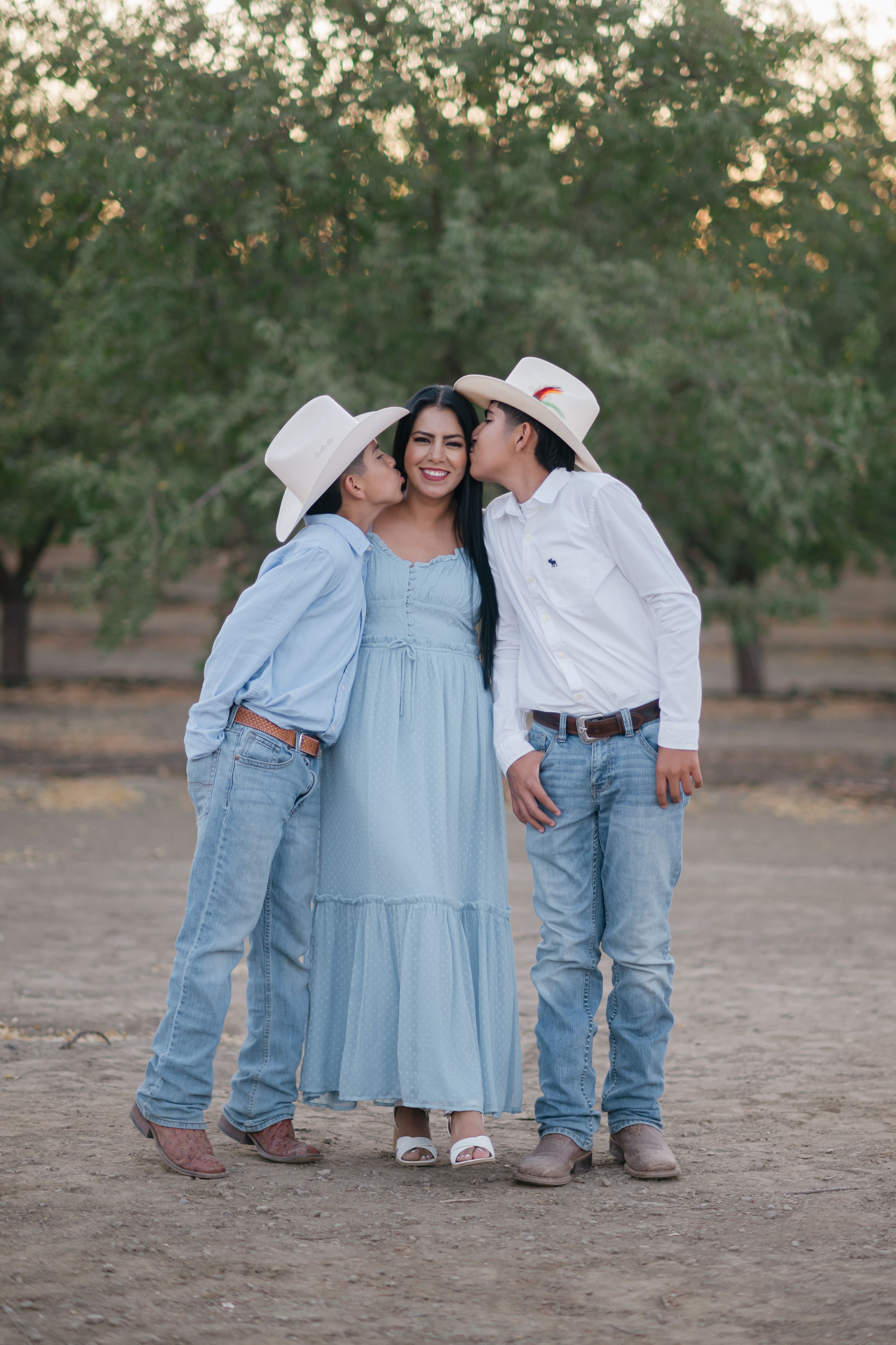 Family wearing denim and light blue dress pose together in rustic outdoor setting during golden hour.