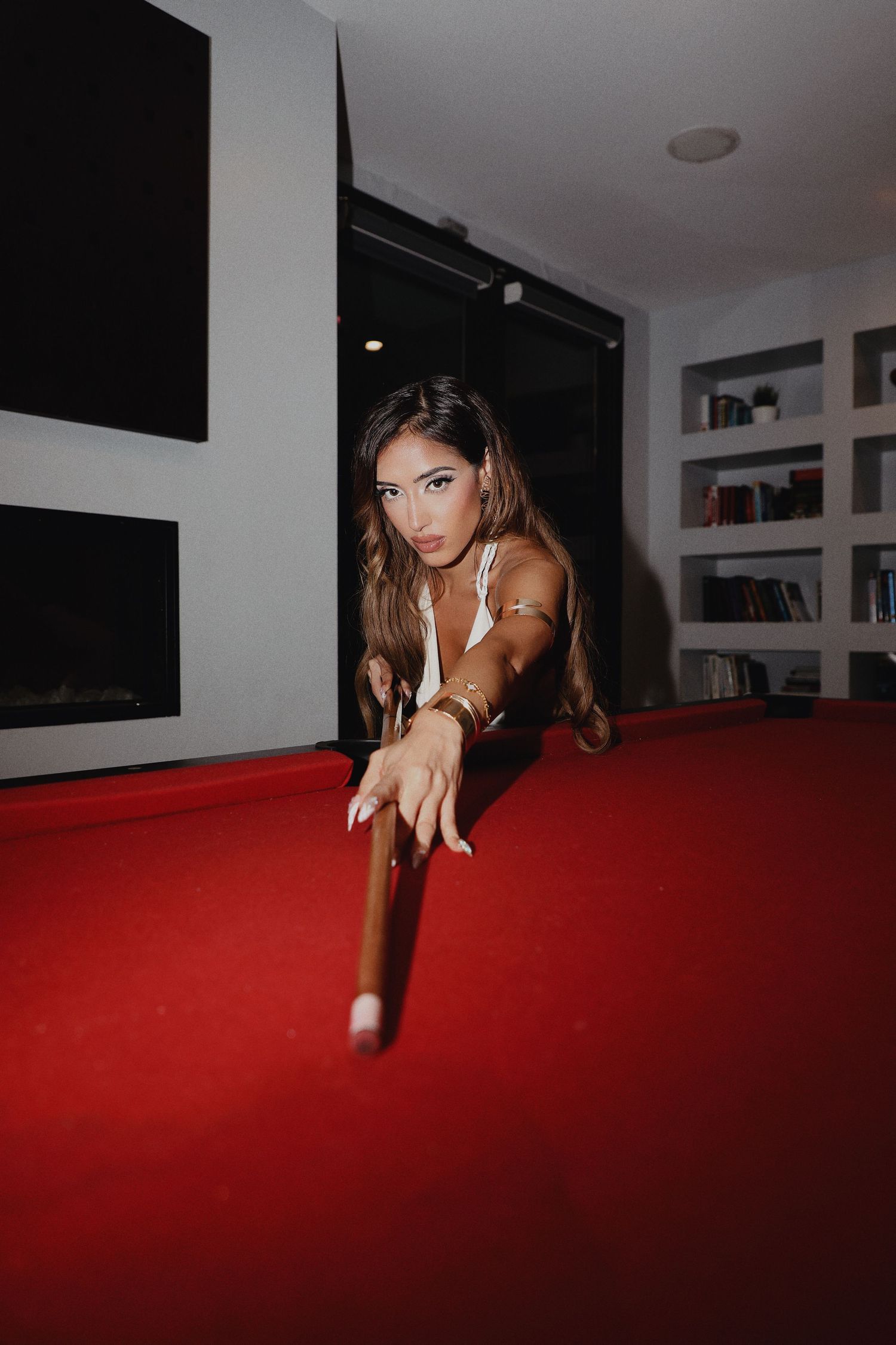 Person in dark room leaning across red pool table surface with dramatic lighting and shadows.