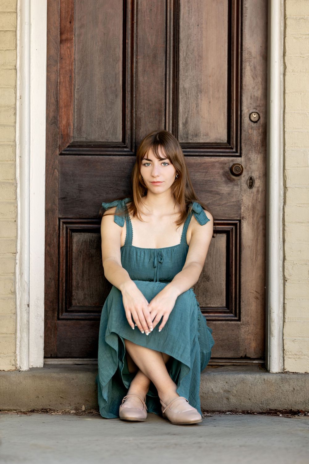 Young woman in teal dress sitting against rustic wooden double doors.
