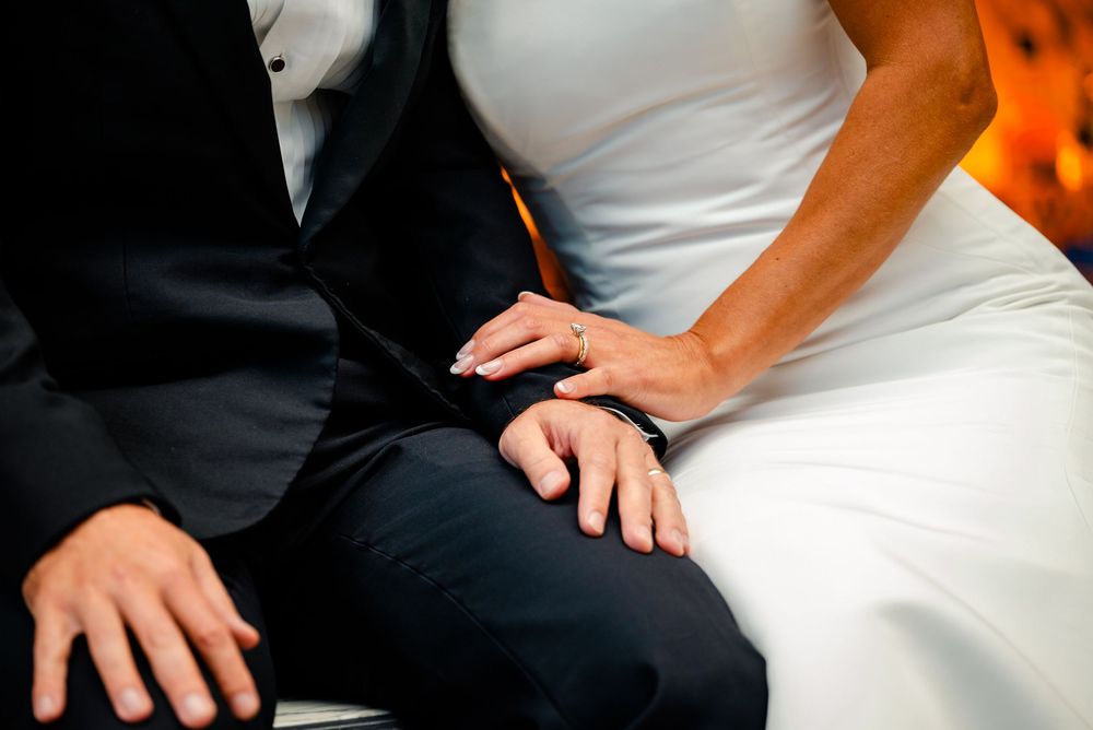 Close-up details of a couple sitting together in formal wedding attire with dramatic lighting.